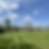 The image showcases a beautifully manicured lawn with precise mowing lines, set against a backdrop of a clear blue sky with scattered clouds. The greenery is punctuated by mature trees, highlighting the serenity and well-maintained landscape of a peaceful outdoor setting.