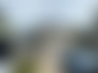 A roofing contractor inspects a two-story residential home with a newly installed dark shingle roof in Fort Walton Beach, Florida. A white work van and blue pickup truck are parked in the driveway, indicating an active roofing project.