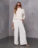 Modelo femenina posando con jersey crema y pantalones palazzo blancos.