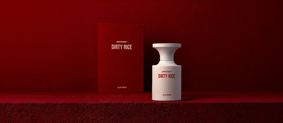 White perfume bottle and red box labeled "Dirty Rice" on a textured red surface with a matching red background. Mood is bold and striking.