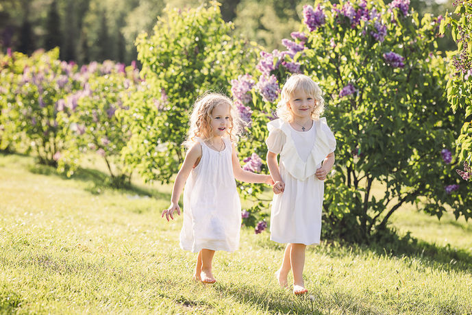 Basos mergaitės baltomis suknelėmis bėga tarp alyvų