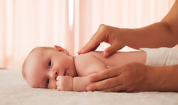 Mother doing massage on her healthy infant baby. Small caucasian newborn laying on his bel