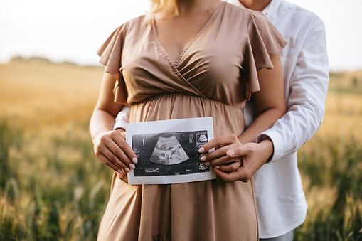 Pregnant woman with husband holding ultrasound baby image. Close-up photo of ultrasound im