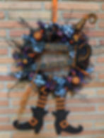 Orange blue and black Halloween wreath with witch hat, witch legs, twig broom, pumpkins, berries, bows and black fabric.