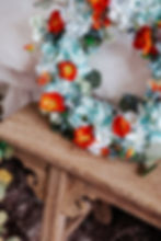 Detail view of blue, white, and orange floral wreath, with poppies, berries, eucalyptus and prairie flowers.