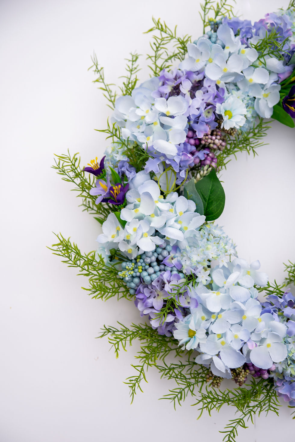 Detail of purple floral greenery wreath with lush hydrangeas, crocus blooms, garden daisies and pip berries.