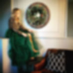 Woman in cheetah print shirt and green dress sitting next to winter greenery wreath with lotus seedpods and pine branches.