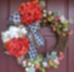 Grapevine wreath with white and red flowers, black and white bow, white berries, cottonseed pods and green leaves.