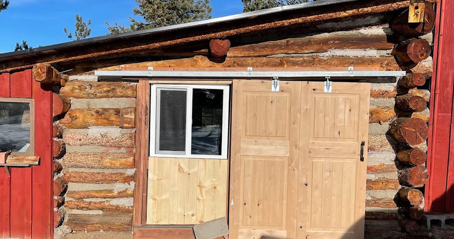 Log cabin exterior with light wooden sliding barn door and window.