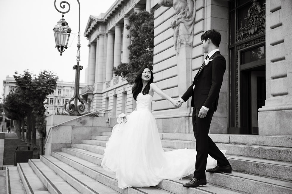 Black-and-white wedding couple holding hands on stone steps outside a City Hall, smiling warmly.