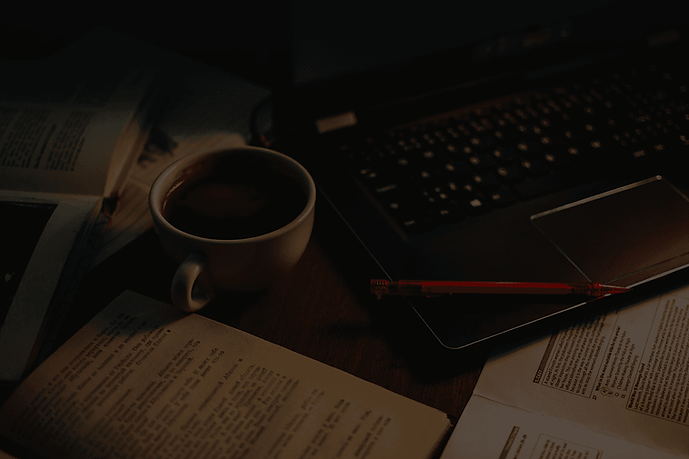 Coffee cup filled with black coffee sitting between a keyboard and an open book.