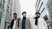 Three menswear buyers in tailored wool coats and leather boots walking through a Milan street during Milan Fashion Week, carrying garment bags and accessories that reflect the SS27 collections shown by Prada, Giorgio Armani, Thom Browne, Dolce Gabbana and Missoni. This look represents the structured, layered silhouettes highlighted in fashion trend forecasting for the season and referenced across the milan fashion week schedule. Brands tracking these trends often rely on a b2b fashion platform and order management clothing tools to move runway concepts into confirmed retailer orders after the show.
