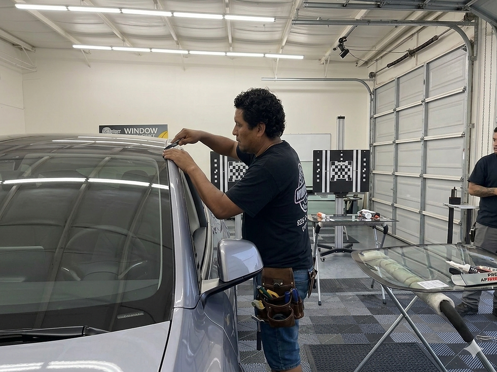 wide-angle photograph taken inside the high-tech, closed-bay calibration facility of Low Price Auto Glass Dublin, featuring the lead technician matching image_2.png build performing a precise final trim on a Girasole Silver Tesla Model Y windshield after installation. The technician wears a branded black t-shirt (image_2.png logo visible) and a professional leather tool belt, viewed from an intimate over-the-hood angle. Specialized linear overhead lighting from image_18.png illuminates the smooth checkered floor and distinct blurred ADAS calibration targets in the background, validating expert technical standards in Dublin, CA. Natural, bubble-free film VLT 50% with perfect edge gap on the side-by-side work stations. Shot with a documentary film grain and high dynamic range.