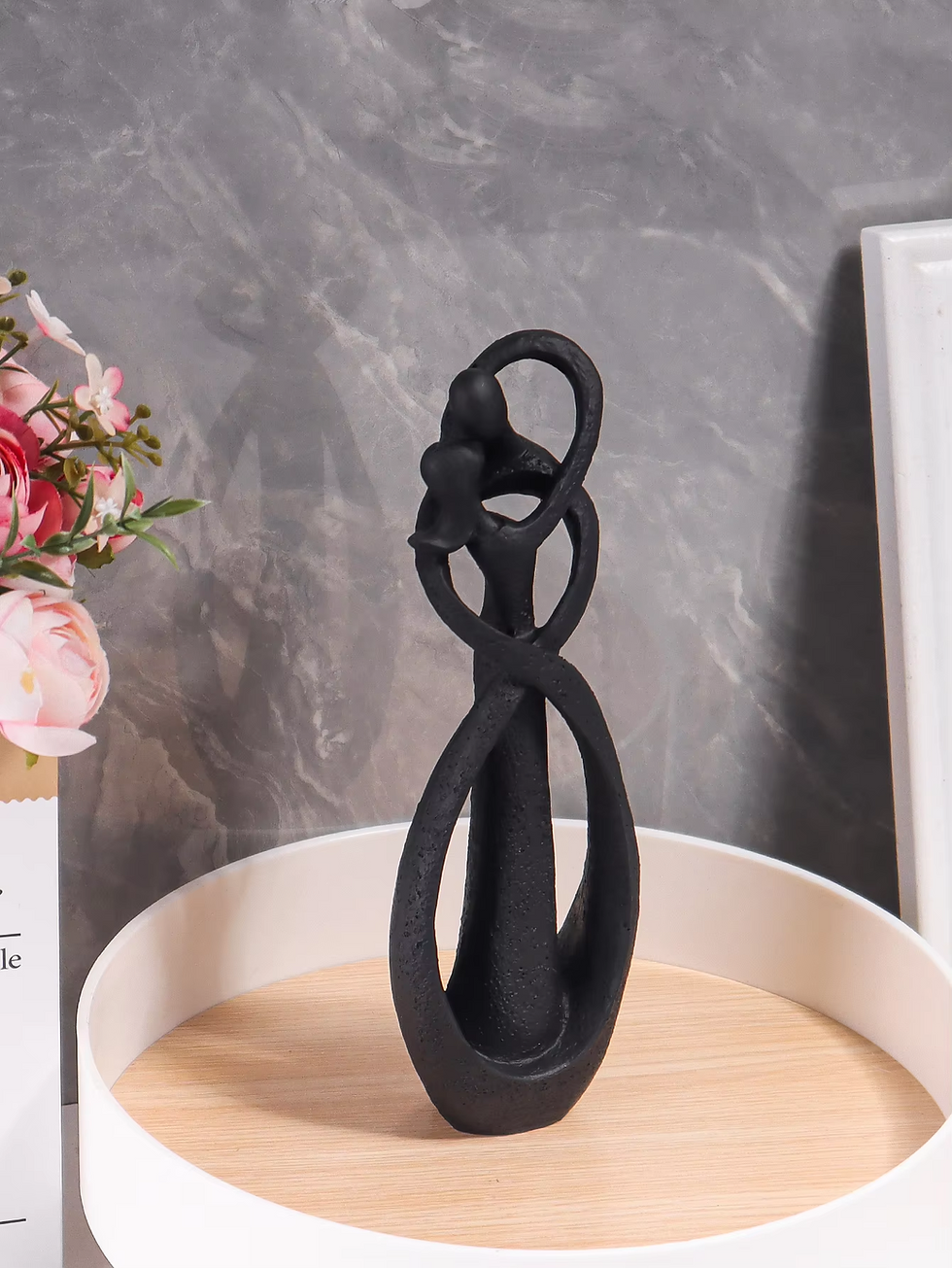 Escultura nórdica preta de casal se abraçando em design abstrato.