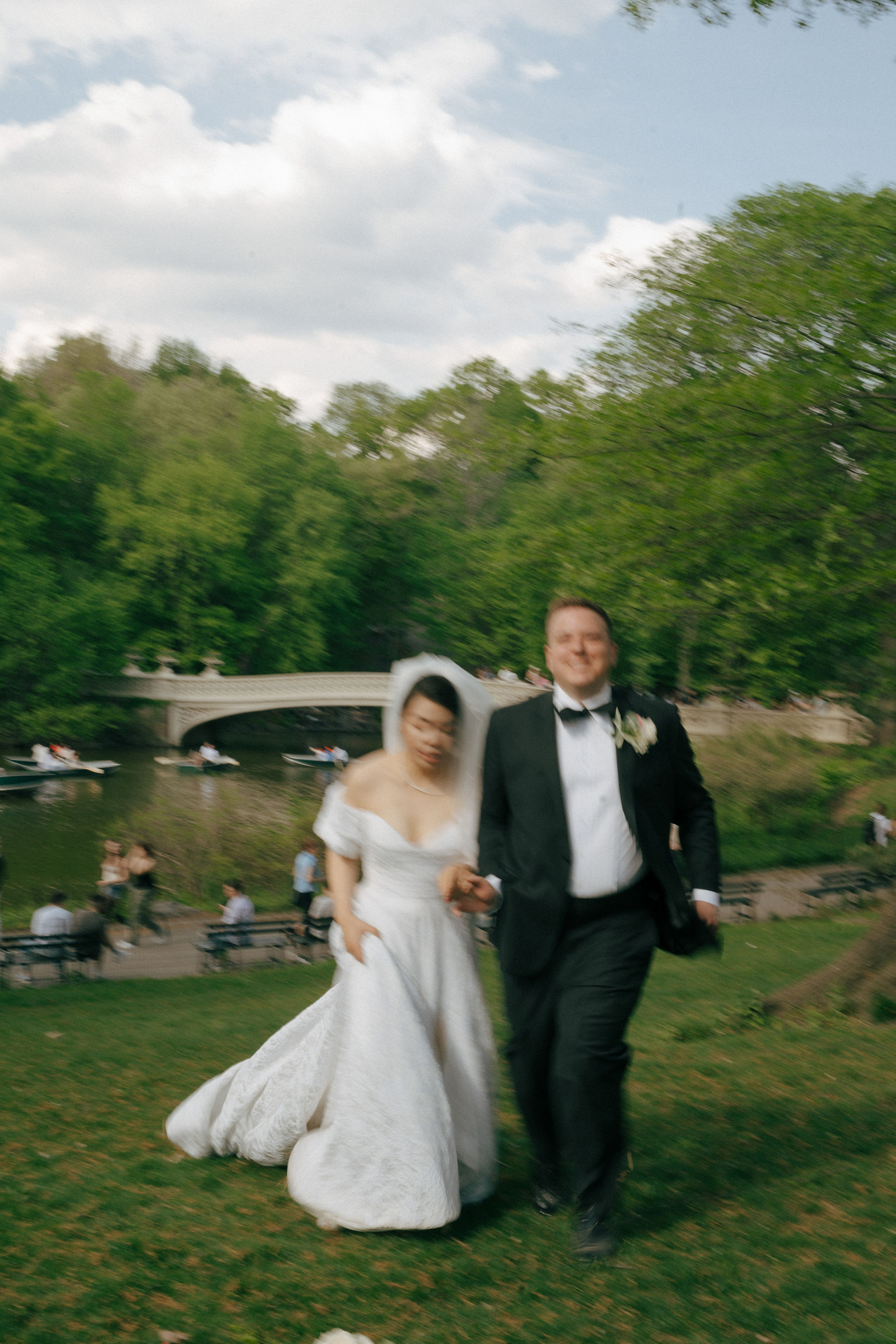 Newlywed couple running and laughing in Central Park during elopement photoshoot at Bow Bridge