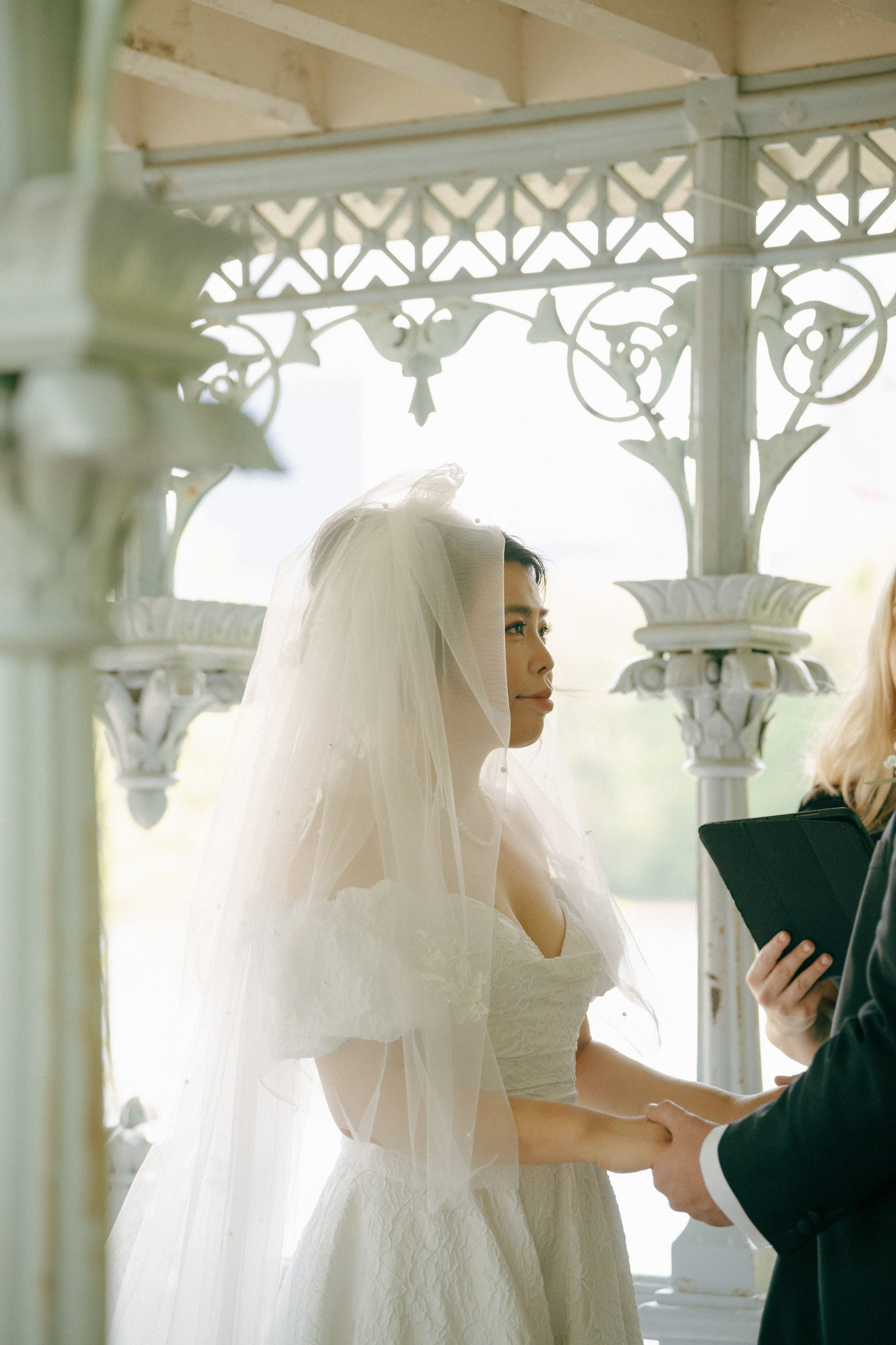 Bride in white dress and veil holding hands with her partner during romantic Ladies Pavilion Central Park wedding, New York elopement photography, spring ceremony photoshoot
