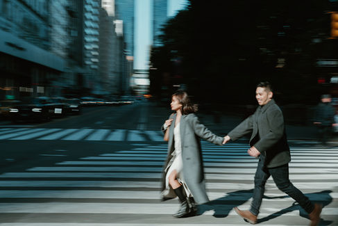 Cinematic couple walking hand in hand across a NYC street during romantic photoshoot in Central Park