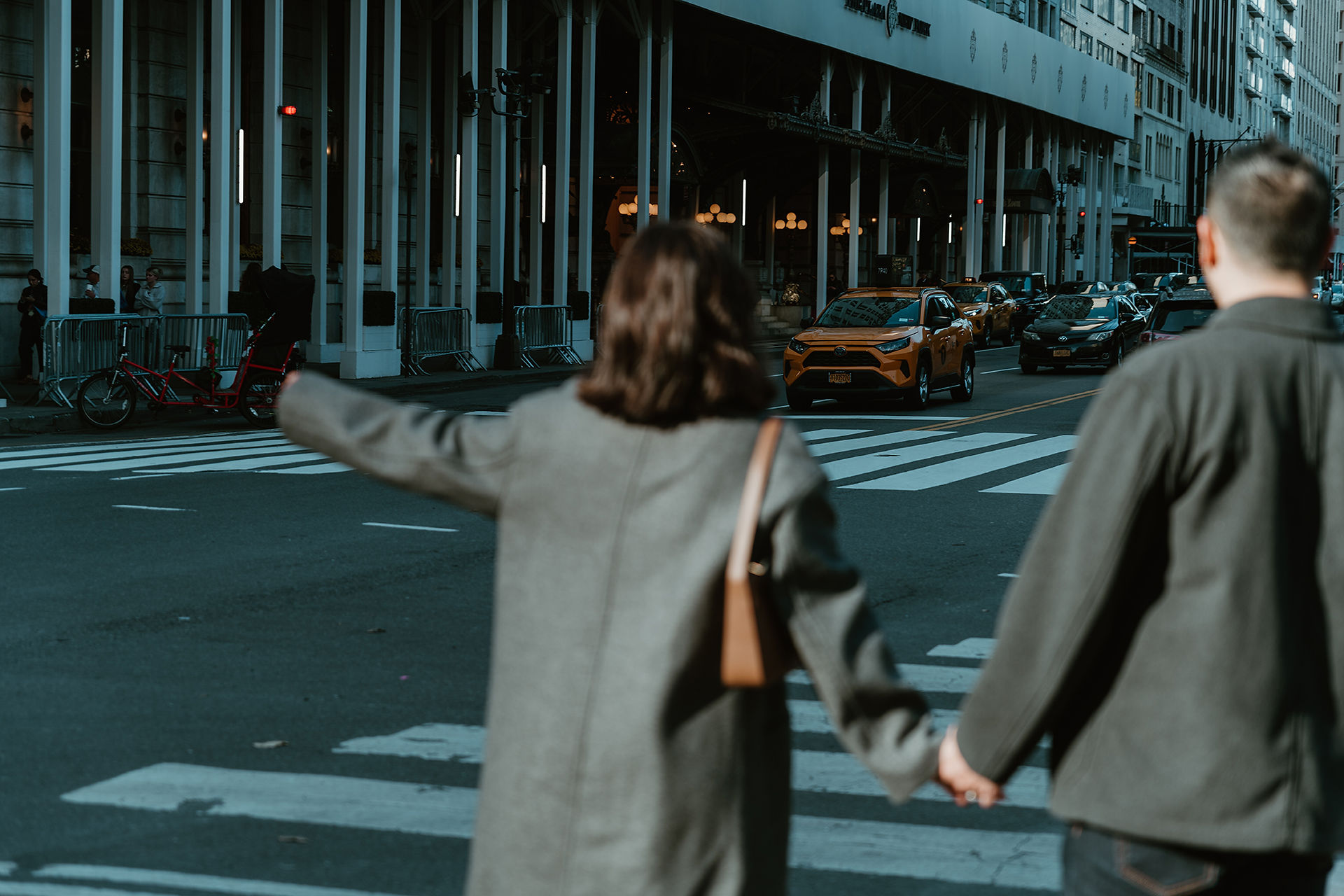 Romantic couple holding hands on a bustling NYC street, as they hail a taxi after their Central Park photoshoot