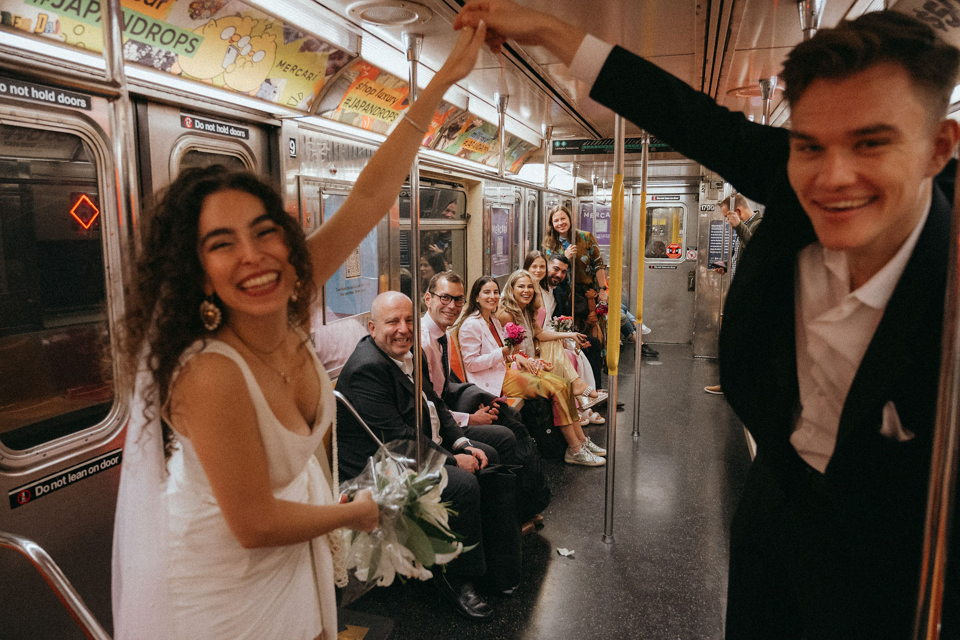 Bride and groom smiling holding hands in NYC subway car wedding photoshoot, Groom and Bride family in the background, on their way to City Hall Elopement