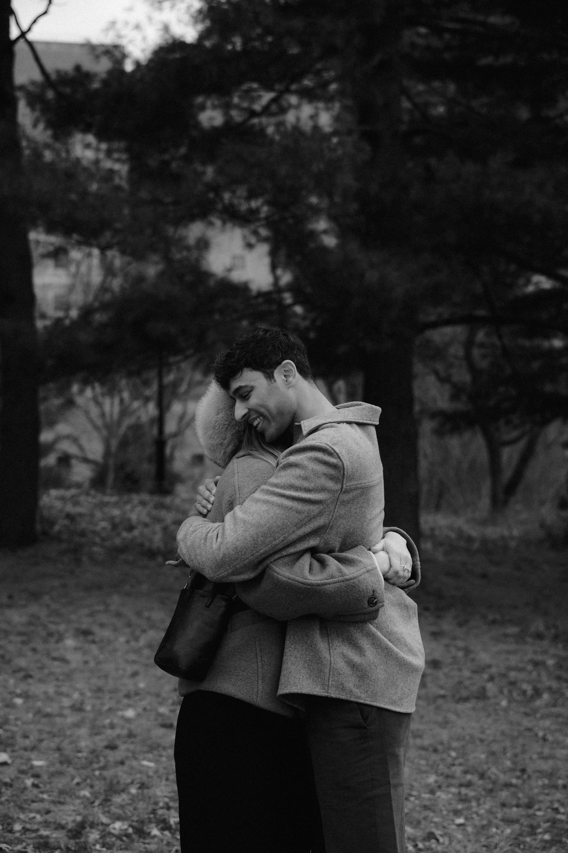 candid romantic couple embracing central park pine trees black and white documentary photography