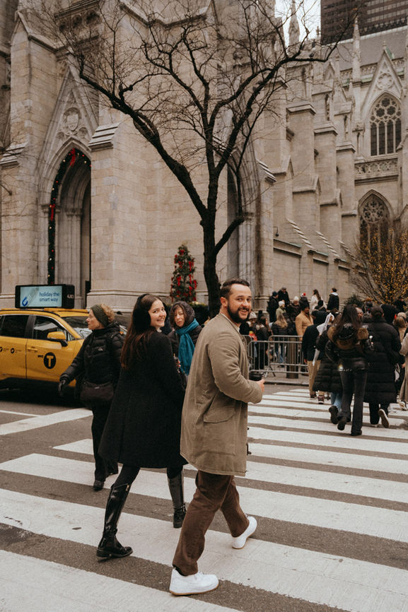 Couple strolling across NYC street with yellow taxi and St patricks cathedral in background during romantic photoshoot