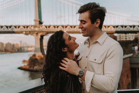 Couple hug on rooftop at Time Out Market in DUMBO with Brooklyn Bridge and skyline views, Brooklyn engagement photographer NYC