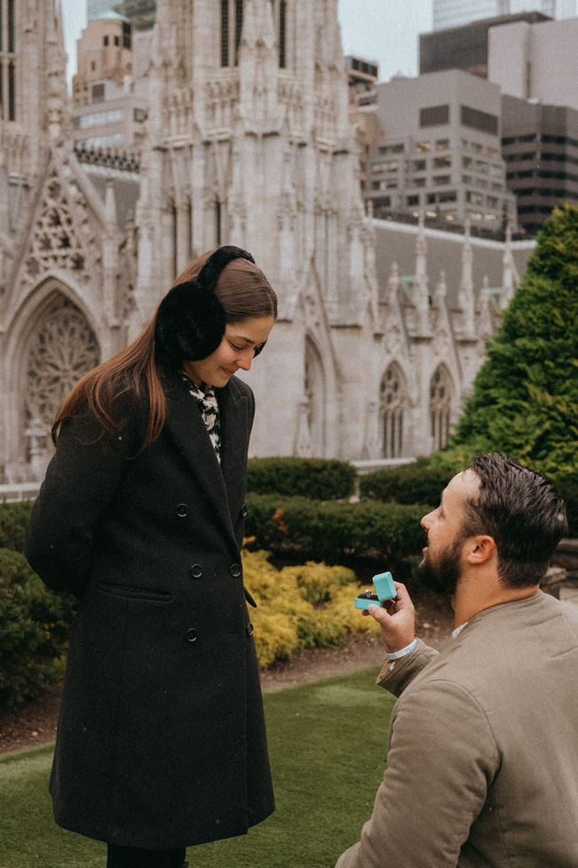 Surprise proposal at 620 Loft and Garden next to Rockefeller Center Garden, with a Tiffany engagement ring, girl looking at the ring smiling, St Patrick’s cathedral portrait photos