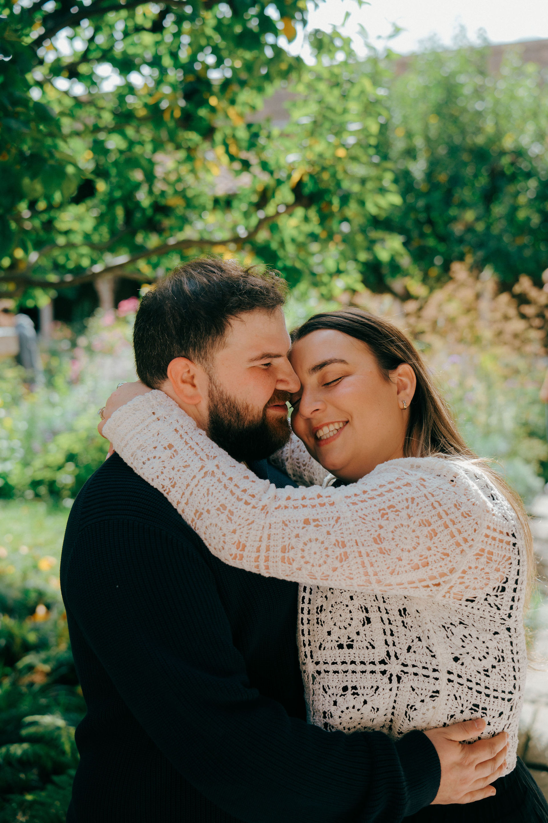 Romantic surprise proposal at the Met Cloisters, dreamy New York photoshoot in lush spring sunlight, happy couple hugging