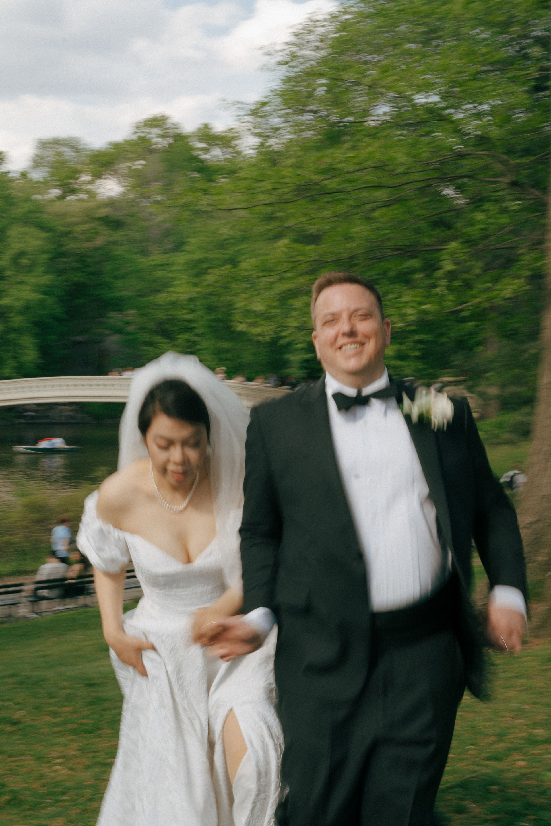 Newlywed couple running and laughing in Central Park during elopement photoshoot at Bow Bridge