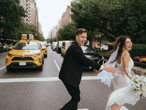 Bride and groom run hand in hand across a busy NYC street, taxis and cars visible for NYC elopement!