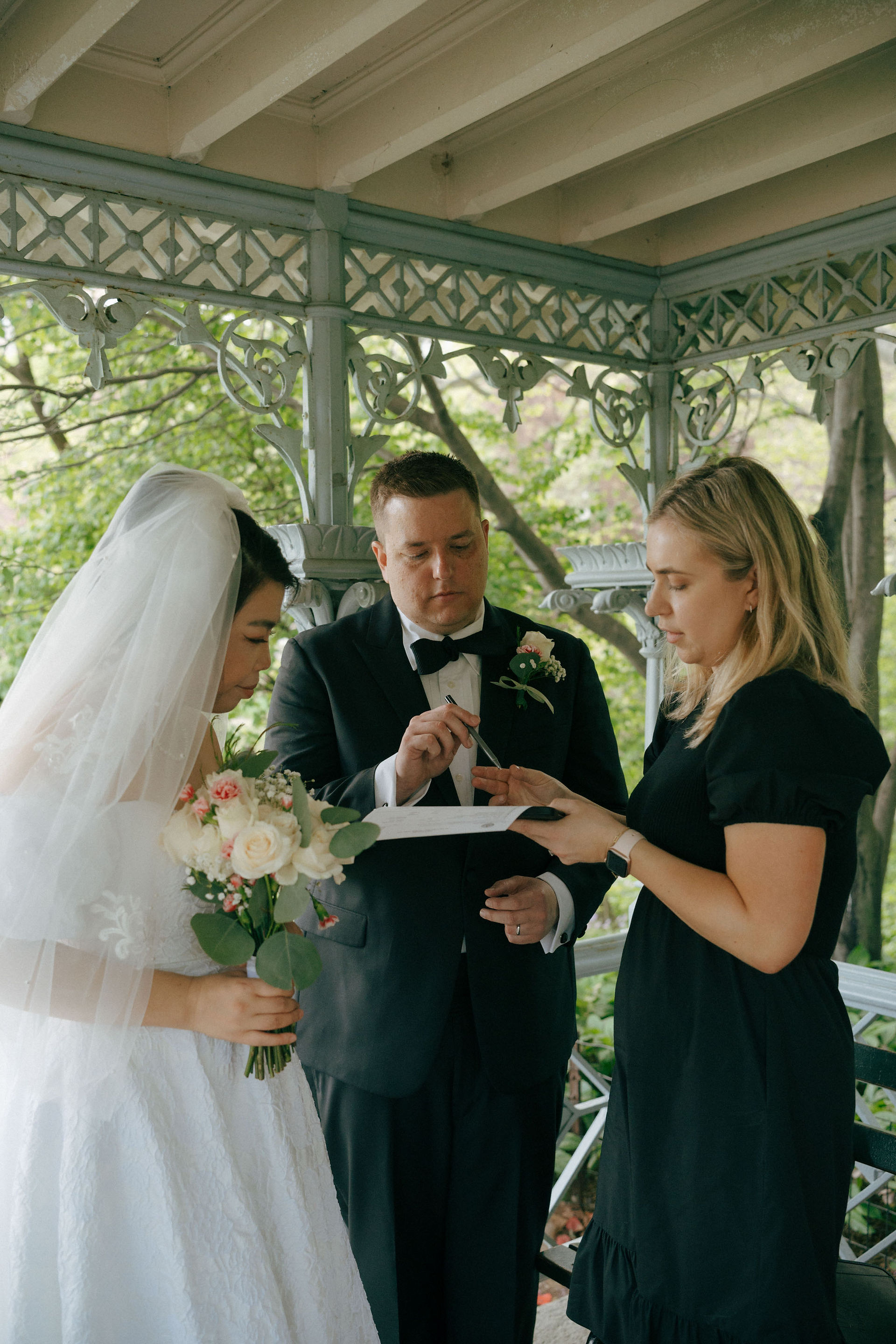 Bride and groom in Central Park signing marriage certificate bouquet in hand during their elopement