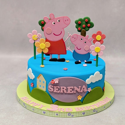 A blue iced cake with hills and houses around side of cake, with Peppa & Gorge stood on top of cake with flowers and tree decorations