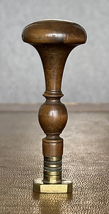 Wooden stamp with a coat of arms showing a dexter armed arm.
