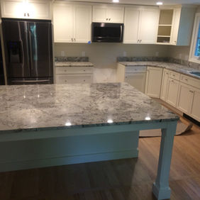 Kitchen with white cabinets, granite counters, island, and fridge
