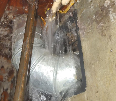 Water actively leaking from a burst or failed pipe joint inside a wall cavity, showing significant water damage and corrosion