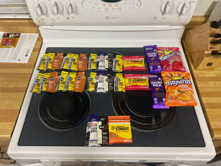 White stovetop in kitchen covered with GU gels, Honey Stinger, Maynards and Cadbury candy packets arranged in rows.