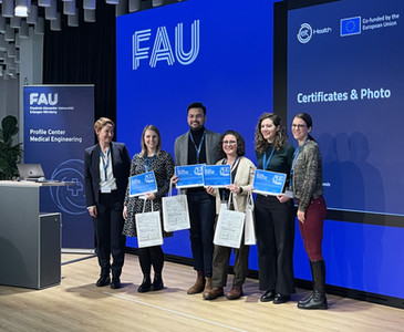 A group of five award recipients and a presenter stand on stage at Friedrich-Alexander-Universität (FAU), smiling and holding certificates. A large blue screen behind them displays the event title, SCI FI program branding, and the EIT Health and European Union logos.