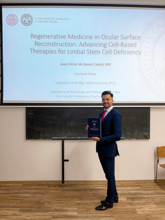 Joao Victor Cabral standing proudly with his doctoral thesis at Charles University, with the thesis title displayed on the projector screen behind him.