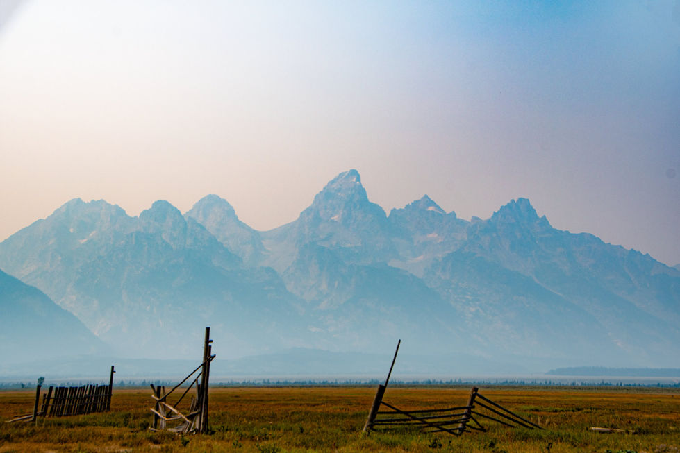 a broken fence in a field with a mountain range in the background at Yellowstone National Park