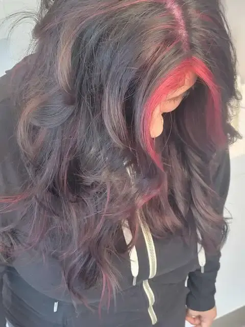 Woman with long dark hair featuring red balayage and soft curls at Blue Iris Salon