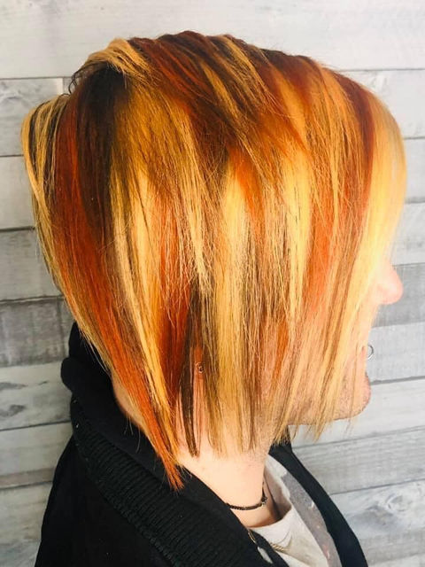 Side view of an angled bob with vibrant streaks of orange, red, and blonde, styled for a striking and edgy appearance.