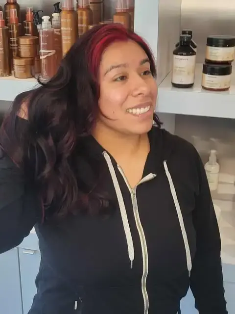 Woman with long dark hair featuring red balayage and soft curls at Blue Iris Salon
