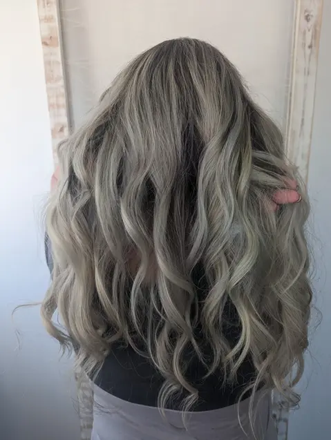 Back view of long, wavy hair with a silver balayage, blending natural roots into cool, smoky ends for a modern and voluminous style.