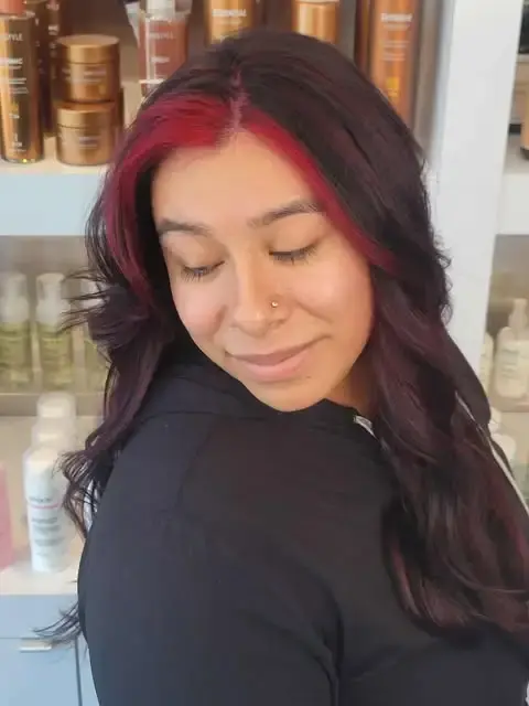 Woman with long dark hair featuring red balayage and soft curls at Blue Iris Salon