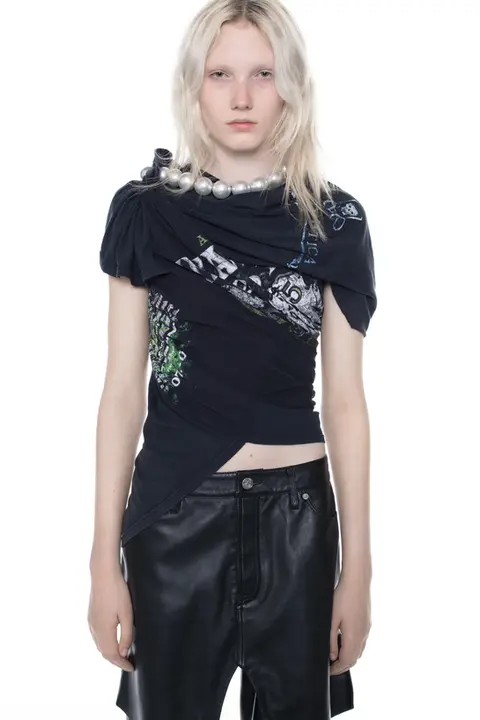 A model wearing a unique, deconstructed top created through expert upcycling of secondhand graphic t-shirts. This circular remake features artistic draping and an asymmetrical silhouette, showcasing high-end craftsmanship. Developed and produced in-house by XV Production in Borås, SwedenA showcase of high-end sustainable fashion and remake expertise, designed and produced in Sweden. This garment highlights circular craftsmanship, utilizing upcycled materials and ethical manufacturing processes. Expertly realized through in-house design development, remake techniques, and local production at XV Production, Borås – driving the transition towards a circular textile industry