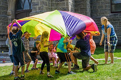 Children gather under a parachute outside in the church yard.