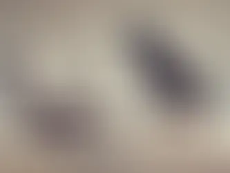 A black crow sits on a wooden stool beside a cream lounge chair in a minimalist room with a wooden floor, creating a mysterious mood.