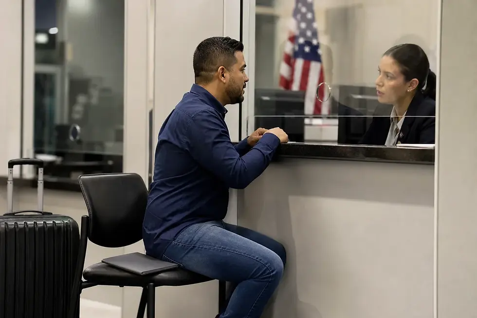 Trabajador independiente colombiano conversa en una ventanilla consular genérica con bandera de Estados Unidos durante el proceso de visa americana.