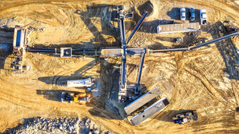 Construction site with partially built structures, equipment, fencing, and open work areas