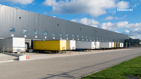 Autonomous drone conducting overnight security patrol over large warehouse distribution center yard with truck trailers and loading docks, perimeter surveillance
